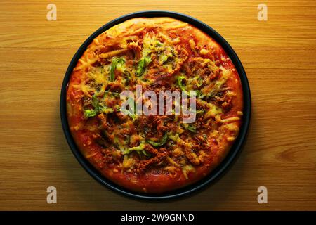 Pizza mit Fleisch und Gemüse auf einem schwarzen Teller auf einem Holztisch Stockfoto