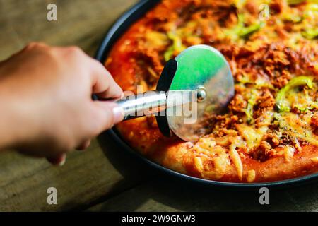 Schneiden Sie Peperoni-Pizza in Scheiben mit einem speziellen Pizzaschneidemesser. Stockfoto