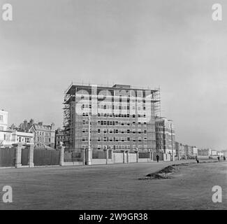 Ein Blick nach Osten entlang der Strandpromenade von King’s Esplanade, Hove, Brighton and Hove, East Sussex, England, UK ca. 1958. Die moderne Entwicklung findet statt, während Flag Court im Bau ist – der Luxusblock mit 54 Wohnungen wurde 1959 fertiggestellt. Es ist abgewinkelt, so dass die meisten Wohnungen einen Blick auf das Meer haben. Hinter diesem Block befindet sich der ältere 1934 Block, Courtenay Gate auf der Courtenay Terrace, Kingsway. Die hinteren Gärten der älteren Häuser der Courtenay Terrace sind auf der linken Seite zu sehen. Hove Council nutzte einen Teil ihrer Gärten, um die Promenade zu vergrößern – ein Vintage-Foto aus den 1950er Jahren. Stockfoto