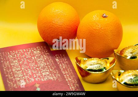 Chinesische Neujahrsdekoration mit Orangen, dunkelroten Päckchen und Goldbarren auf gelbem Deckgrund. Chinesisches Weihnachtskonzept. Stockfoto