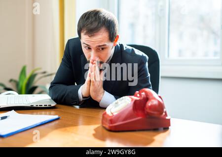 Porträt eines Geschäftsmannes, der auf das Telefon blickt und für einen Anruf betet Stockfoto