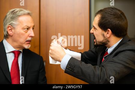 Ein wütender Geschäftsmann zerreißt ein Dokument vor seinem Kollegen Stockfoto