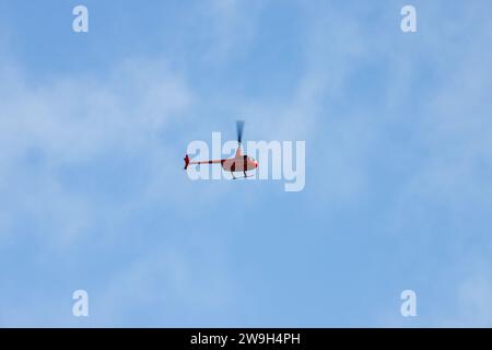 Kleiner roter ziviler Hubschrauber steht an einem sonnigen Tag am Himmel Stockfoto