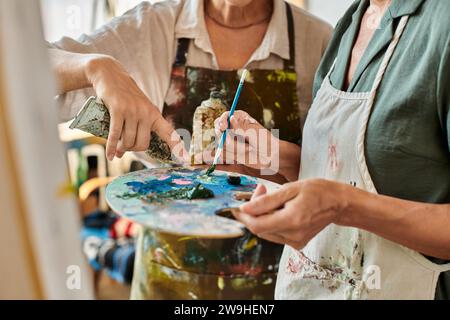 Zugeschnittene Ansicht reifer Frauen in Schürzen, die Farben auf Palette während des Meisterkurses in Kunstwerkstatt mischen Stockfoto