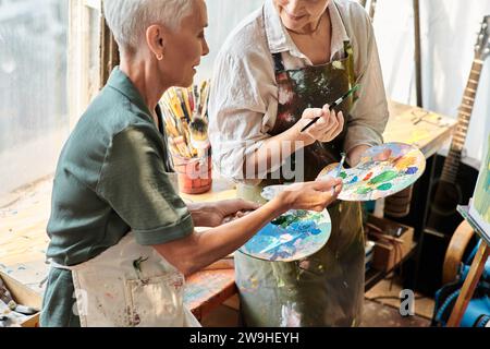 Reife Malerinnen mischen Farben auf der Palette während des Meisterkurses in der Handwerkstatt, Hobby Stockfoto