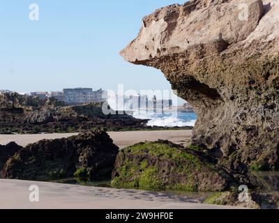 Wellen stürzen in der Nähe großer Felsen an einem Sandstrand mit der Medina in der Stadt Essaouira, Marokko. Dezember 2023 Stockfoto