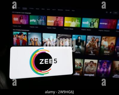 Person, die ein Mobiltelefon mit dem Logo der indischen Video-Streaming-Plattform ZEE5 vor der Business-Webseite hält. Schwerpunkt auf dem Display des Telefons. Stockfoto