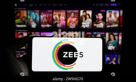 Person, die ein Mobiltelefon mit dem Logo der indischen Video-Streaming-Plattform ZEE5 vor der Business-Webseite hält. Schwerpunkt auf dem Display des Telefons. Stockfoto