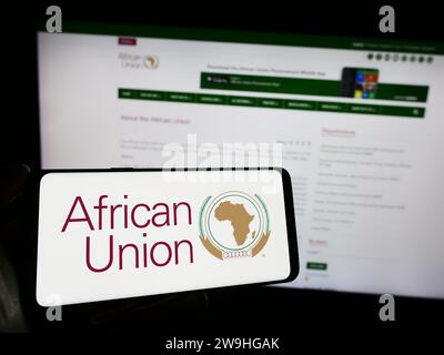 Person, die ein Mobiltelefon mit dem Logo der kontinentalen Organisation Afrikanische Union (AU) vor der Webseite hält. Schwerpunkt auf dem Display des Telefons. Stockfoto