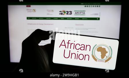 Person mit Mobiltelefon mit Logo der kontinentalen Organisation African Union (AU) vor der Webseite. Schwerpunkt auf dem Display des Telefons. Stockfoto