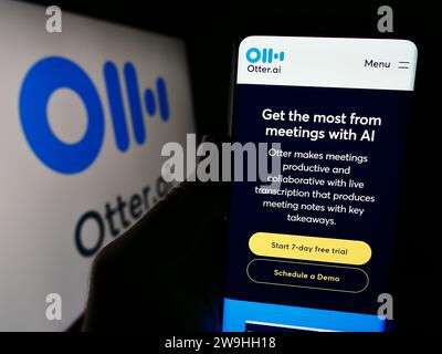 Person, die ein Handy hält, mit Webseite des US-amerikanischen Unternehmens für künstliche Intelligenz Otter.ai Inc. Vor dem Logo. Konzentrieren Sie sich auf die Mitte des Telefondisplays. Stockfoto