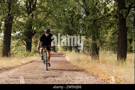 Junger Radfahrer mit Helm und Brille fährt auf der Landstraße mit dem Fahrrad. Ein sportlicher Kerl auf einem Schotterrad liebt das Training an der frischen Luft. Stockfoto