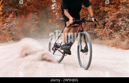 Radfahrer auf Radtouren entlang der Schotterstraße, die Staub vom Hinterrad im Herbstwald sammelt. Schotterradfahren. Extremsport- und Aktivitätskonzept. Stockfoto