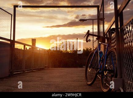 Ein Rennrad steht in der Nähe des Zauns. Fahrradsilhouette auf dem Himmelhintergrund bei Sonnenuntergang. Wunderschöne Landschaft. Stockfoto