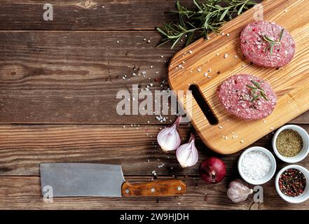 Rohe Fleischkoteletts für einen Hamburger. Rohe Burger. Frisches Bio-Fleisch, Gewürze, Zwiebeln, Knoblauch und Rosmarin auf hölzernem Hintergrund. Blick von oben. Obere V Stockfoto