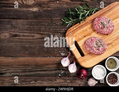 Rohe Burger. Frisches rohes Bio-Fleisch, Gewürze, Zwiebeln, Knoblauch und Rosmarin auf hölzernem Hintergrund. Blick von oben. Draufsicht. Kopierbereich für Text. Stockfoto