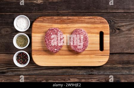 Rohe Bio-Fleischkoteletts für Hamburger auf hölzernem Schneidebrett. Teller mit Gewürzen. Draufsicht. Stockfoto