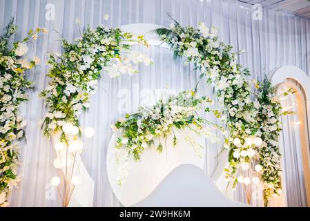Minimalistische Hochzeitsdekoration in weißen Tönen mit grünen Papierblumen, weißem Sofasessel und dekoriert mit Lichtern, indonesische Hochzeit Stockfoto