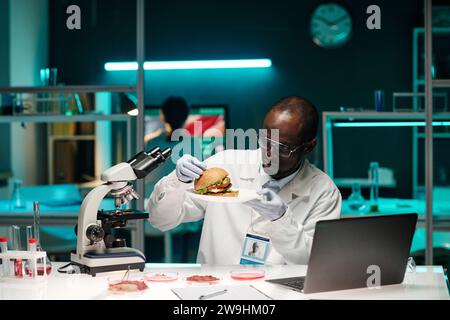 afroamerikanischer Wissenschaftler untersucht Hamburger mit im Labor angebautem Fleisch an seinem Arbeitsplatz im Labor Stockfoto