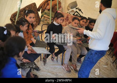 Rafah, Palästinensische Gebiete. Dezember 2023. Der palästinensische Englischlehrer Tariq al-Annabi (R) gewährt es sich weiterhin, Kindern, die mit ihren Familien Zuflucht an der Abu Youssef Al-Najjar Schule suchten, Englisch zu unterrichten. Während der Krieg gegen Gaza andauert, setzen Kinder ihre Ausbildung unter schwierigen Bedingungen fort, da im Gazastreifen keine Bildungsmittel vorhanden sind. Quelle: Mohammed Talatene/dpa/Alamy Live News Stockfoto