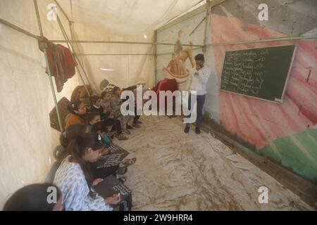 Rafah, Palästinensische Gebiete. Dezember 2023. Der palästinensische Englischlehrer Tariq al-Annabi (R) gewährt es sich weiterhin, Kindern, die mit ihren Familien Zuflucht an der Abu Youssef Al-Najjar Schule suchten, Englisch zu unterrichten. Während der Krieg gegen Gaza andauert, setzen Kinder ihre Ausbildung unter schwierigen Bedingungen fort, da im Gazastreifen keine Bildungsmittel vorhanden sind. Quelle: Mohammed Talatene/dpa/Alamy Live News Stockfoto