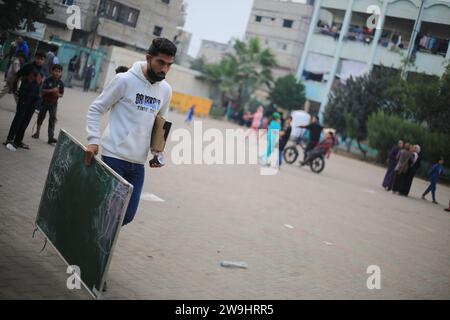 Rafah, Palästinensische Gebiete. Dezember 2023. Der palästinensische Englischlehrer Tariq Al-Annabi trägt eine Tafel auf seinem Weg, um Kindern, die mit ihren Familien Zuflucht suchten, Englisch zu unterrichten. Während der Krieg gegen Gaza andauert, setzen Kinder ihre Ausbildung unter schwierigen Bedingungen fort, da im Gazastreifen keine Bildungsmittel vorhanden sind. Quelle: Mohammed Talatene/dpa/Alamy Live News Stockfoto