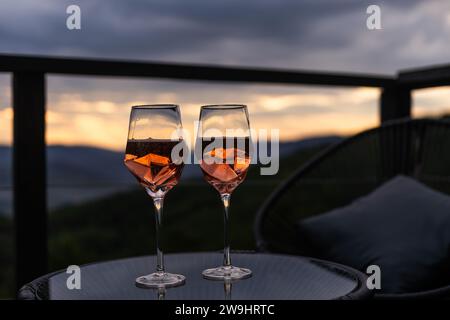 Champagner- und Cocktailgläser auf dem Glastisch auf der Außenterrasse mit Blick auf die Berge bei Sonnenuntergang Stockfoto