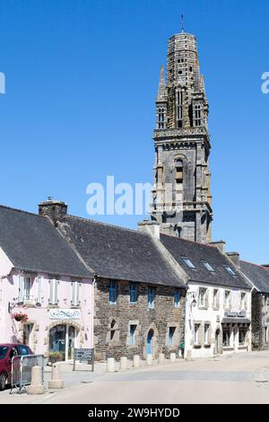 Lampaul-Guimiliau, Frankreich - 09. Juli 2022: Die Kirche Notre-Dame mit ihrem getürmten Glockenturm mit Blick auf die Häuser der Stadt. Stockfoto