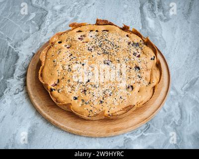 Hausgemachte Kirschtorte mit Sesamsamen auf einem runden Schneidebrett auf einer Marmorplatte Stockfoto