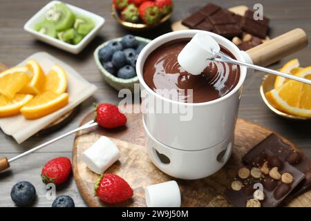 Süßes Marshmallow in Fonduetopf mit geschmolzener Schokolade am Holztisch tauchen Stockfoto