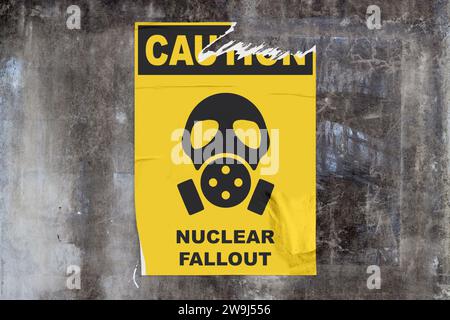 Vollrahmen-Wand aus verwittertem Beton mit einem gerissenen gelben Poster in der Mitte, auf dem eine Gasmaske mit der Aufschrift „Vorsicht - nukleare Fallout“ dargestellt ist. Stockfoto