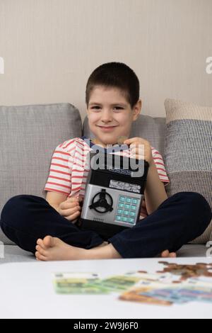 Ein kleiner Junge steckt eine Münze in eine sichere Schweinebank. Finanzkompetenz für Kinder. Stockfoto