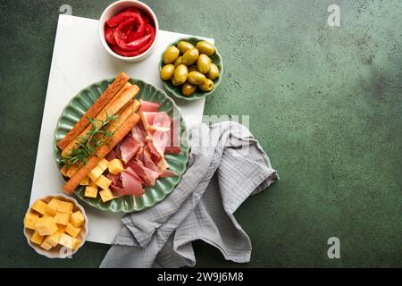 Schinkenscheiben oder Marmeladen. Köstliche grissini-Sticks mit Schinken, Käse, Rosmarin, Oliven auf grüner Platte auf dunklem Hintergrund. Vorspeisentisch Stockfoto