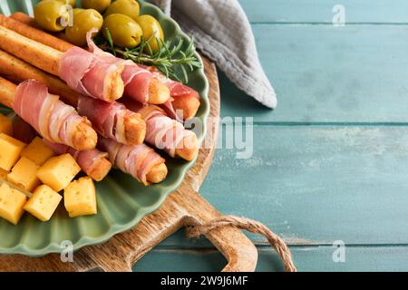 Schinkenscheiben oder Marmeladen. Köstliche grissini-Sticks mit Schinken, Käse, Rosmarin, Oliven auf grüner Platte auf dunklem Hintergrund. Vorspeisentisch Stockfoto