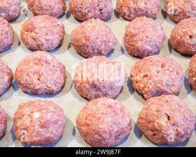 Köstliche Fleischbällchen, ordentlich auf einem mit Pergamentpapier ausgelegten Blech angeordnet, bereit für den ersten Backofen vor dem Frittieren. Stockfoto