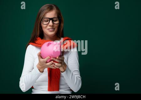 Süße junge Frau mit Brille, die einen weißen Rollkragen trägt und eine Schweinebank hält Stockfoto