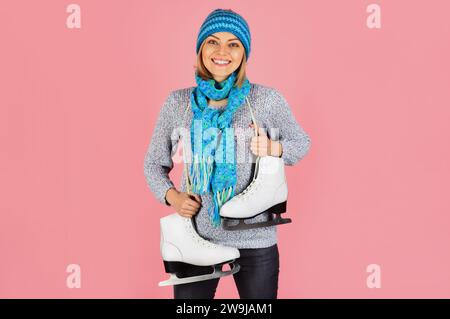 Lächelndes Mädchen in Strickpullover, Schal und Hut mit Schlittschuhen. Wintersportaktivitäten. Hübsche Frau in warmer Kleidung mit Schlittschuhen, die bereit sind Stockfoto