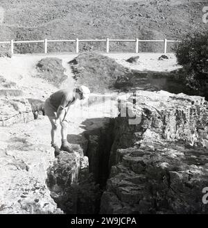 1960er Jahre, historisch, sommerlich und ein Mann, der im Peak District spaziert und auf eine Lücke oder Spalte in einer Felswand blickt, England, Großbritannien. Stockfoto