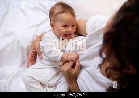 Authentisches Lifestyle-Porträt einer multiethnischen glücklichen Frau Mutter, die ihren kleinen Jungen kuschelt und zusammen auf dem Bett im Schlafzimmerinnenraum sitzt. Menschen. M Stockfoto