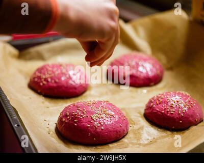 Rote-Bete-Burger-Brötchen auf einem Backblech werden mit Sesamsamen bestreut Stockfoto