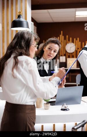Der professionelle Concierge hilft Seniorinnen in der Hotellobby und sorgt für einen reibungslosen Check-in. Die Rezeptionistin bietet älteren Reisenden freundlichen Service, während sie Reservierungsformulare unterschreibt. Stockfoto