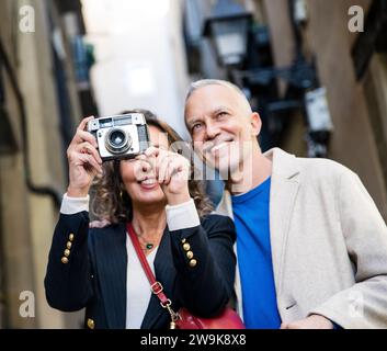 Seniorenpaar, das Fotos mit einer alten Kamera in der Altstadt macht. Mittelerwachsene Frau fotografiert mit ihrem Mann auf der Straße während einer Stockfoto