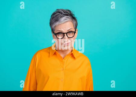 Foto einer verdächtigen misstrauischen Geschäftsfrau, alte Großmutter, die Augenbrauen hebt, tragen ein orangefarbenes Hemd, isoliert auf aquamarinfarbenem Hintergrund Stockfoto