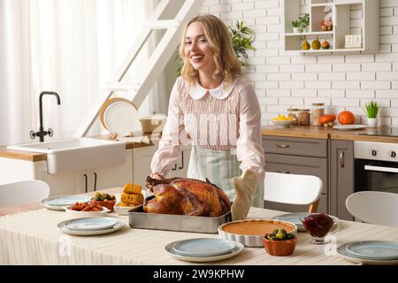 Schöne junge Frau mit leckerem gebackenem truthahn am Tisch in der Küche. Thanksgiving-Feiertag Stockfoto
