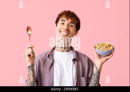 Mann hält Schüssel mit Müsliringen und Löffel auf rosa Hintergrund Stockfoto