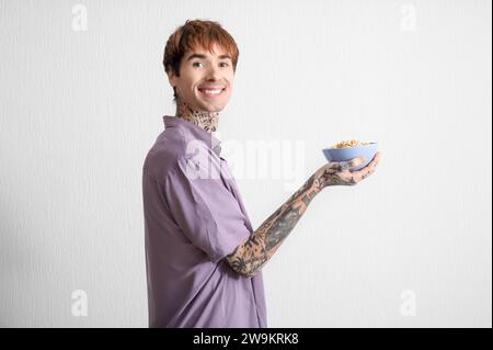 Mann, der eine Schüssel mit Müsliringen auf weißem, strukturiertem Hintergrund hält Stockfoto