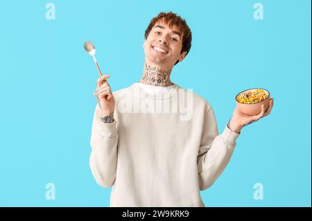 Mann hält Schüssel mit Müsliringen und Löffel auf blauem Hintergrund Stockfoto