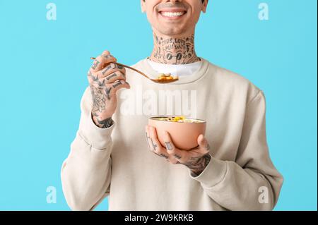 Mann hält Schüssel mit Müsliringen und Löffel auf blauem Hintergrund Stockfoto