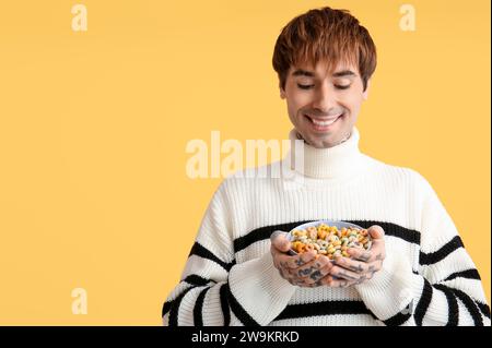 Mann, der eine Schüssel mit Müsliringen auf gelbem Hintergrund hält Stockfoto