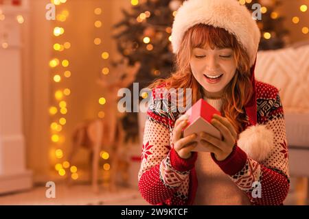 Junge Frau mit Weihnachtsmütze und Adventskalender zu Hause am Weihnachtsabend Stockfoto